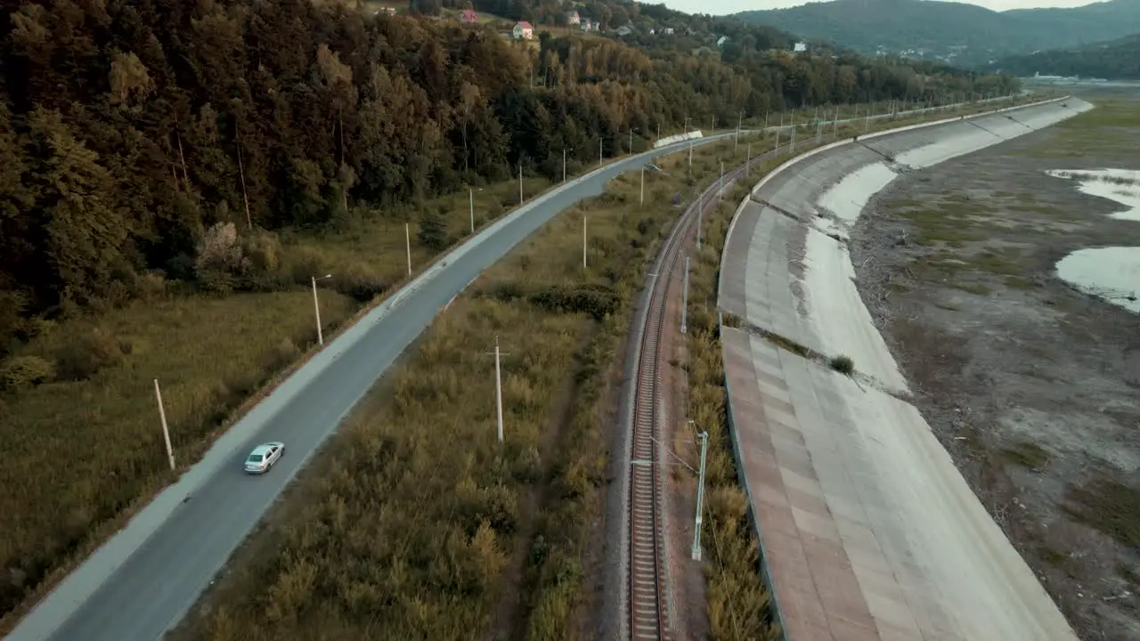 Aerial shot of silver car driving along the railway and dry lake