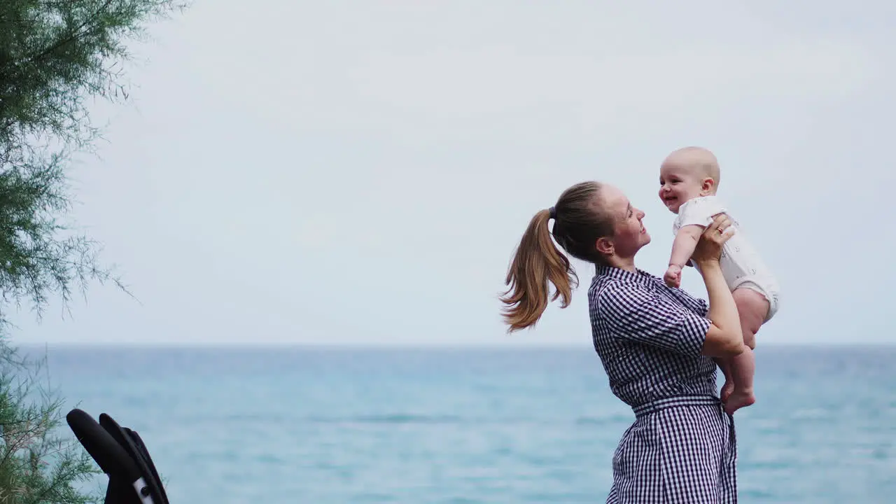 A La Orilla Del Mar La Madre Lanza Juguetonamente A Su Hijo Al Aire Fomentando Un Ambiente Alegre Junto A Las Olas Una Familia Joven Saborea Su Tiempo Junto Al Mar