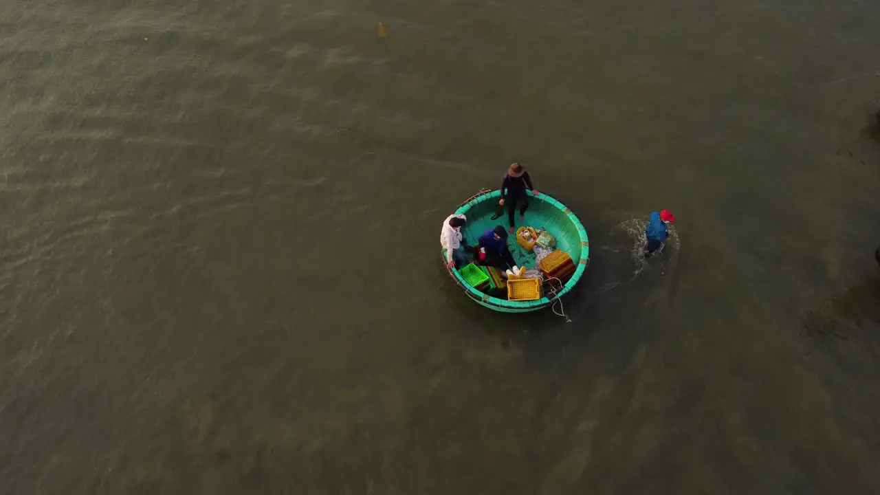 Group of Vietnamese fishermen preparing for fishing trip in round traditional boat aerial drone shot