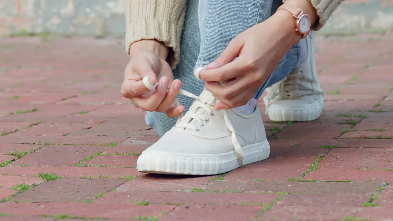 Hands of woman tie shoes or sneakers on pavement