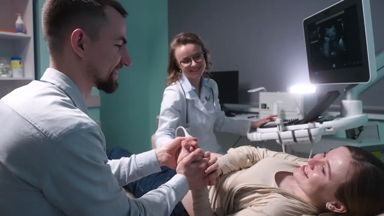 Pregnant Woman Having Ultrasound Scan At The Gynecologist Office While Loving Husband Holding Her Hand 8