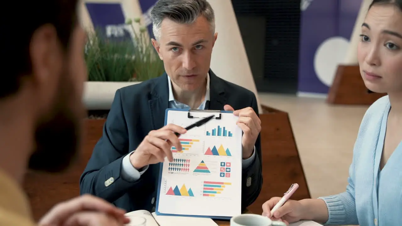 A Work Team Discusses Details Of Some Data In A Report In A Coffee Shop