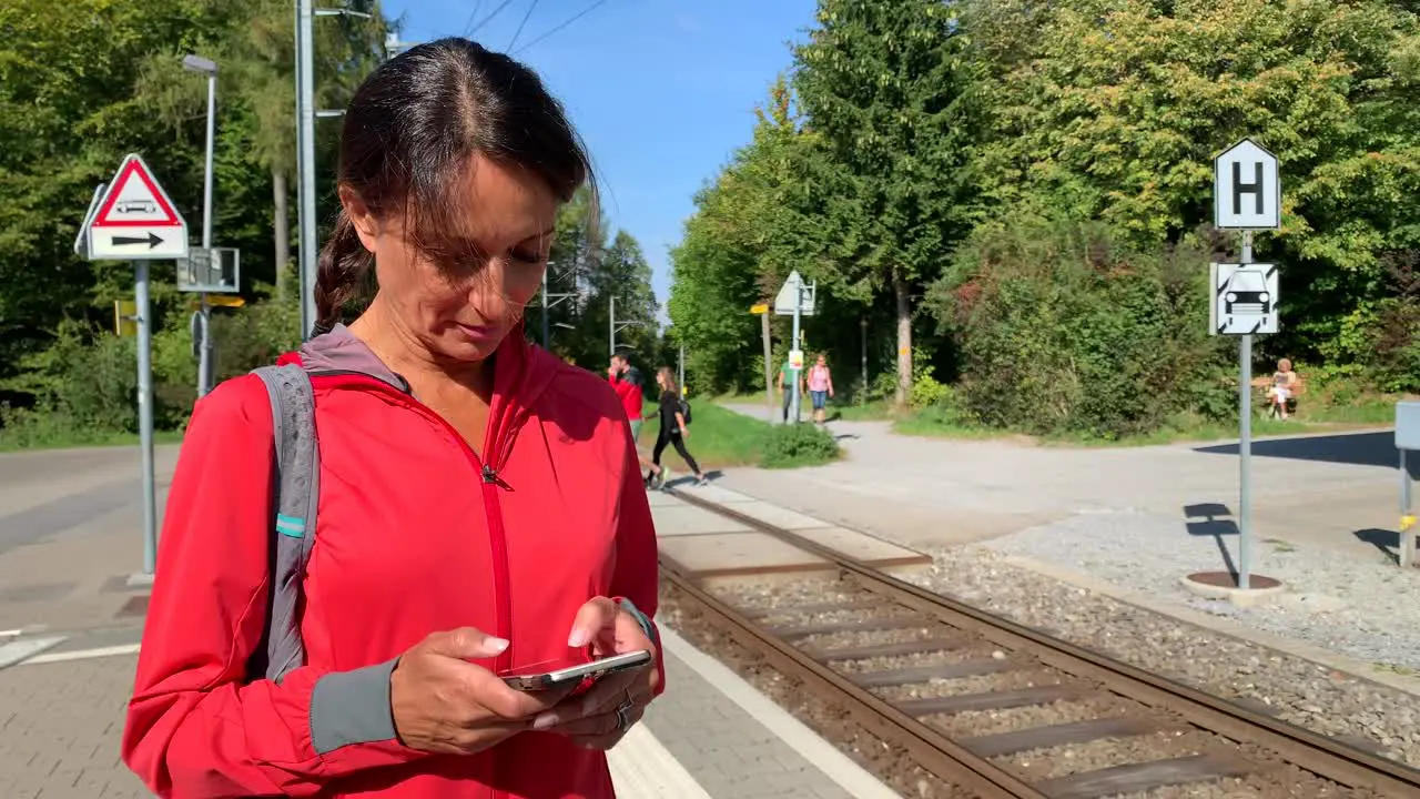 Sporty older woman looking at her phone while waiting for the train facing the camera