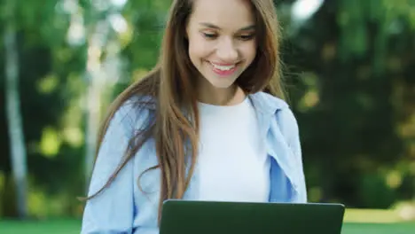 Smiling woman working on laptop computer in city park at summer day