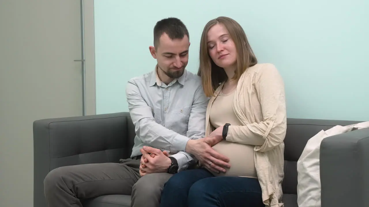 Loving Pregnant Couple Sitting In Waiting Room For A Gynecological Consultation