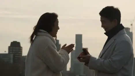 Young Asian Couple With Romantic Man Proposing To Woman Against City Skyline