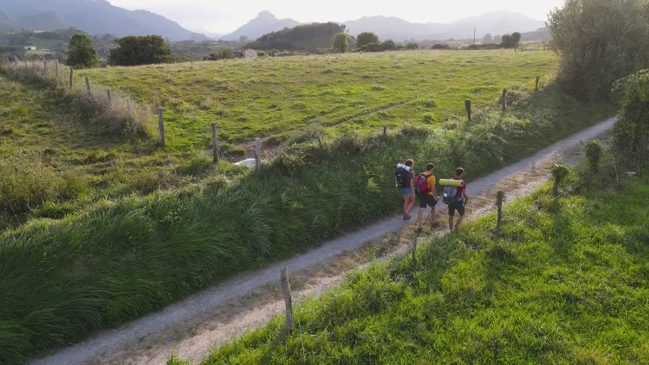 Group Of Three Young Pilgrims Walking Together On Dirt Road On A Windy Summer Day