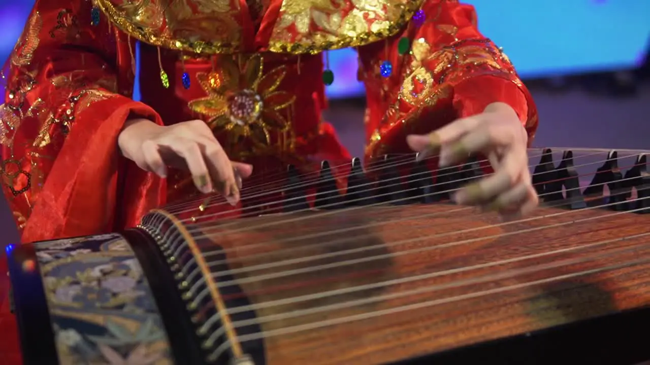 A woman in an ornate red dress plays a traditional Thai string instrument in Bangkok