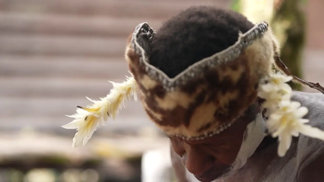 an old man wearing traditional Papuan clothing is carving a wooden carving typical of the Asmat art of Papua Indonesia