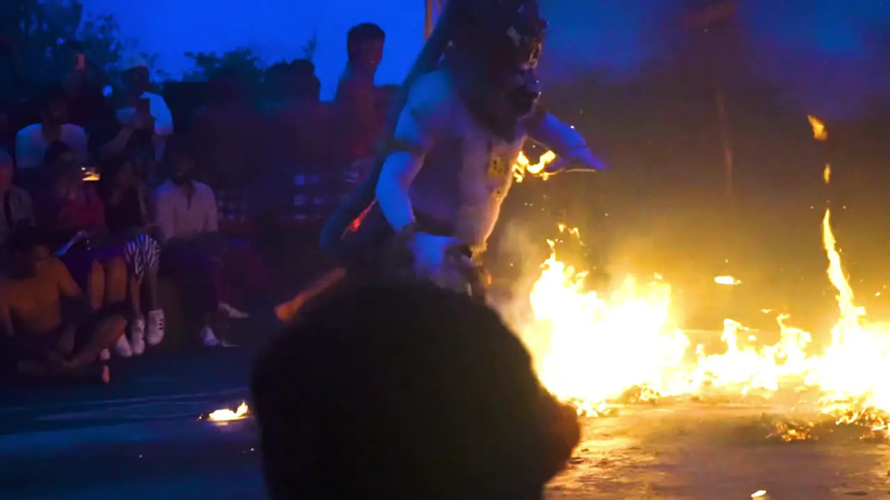 Handheld shot of Balinese cultural fire dance of characters kicking flames during nightfall