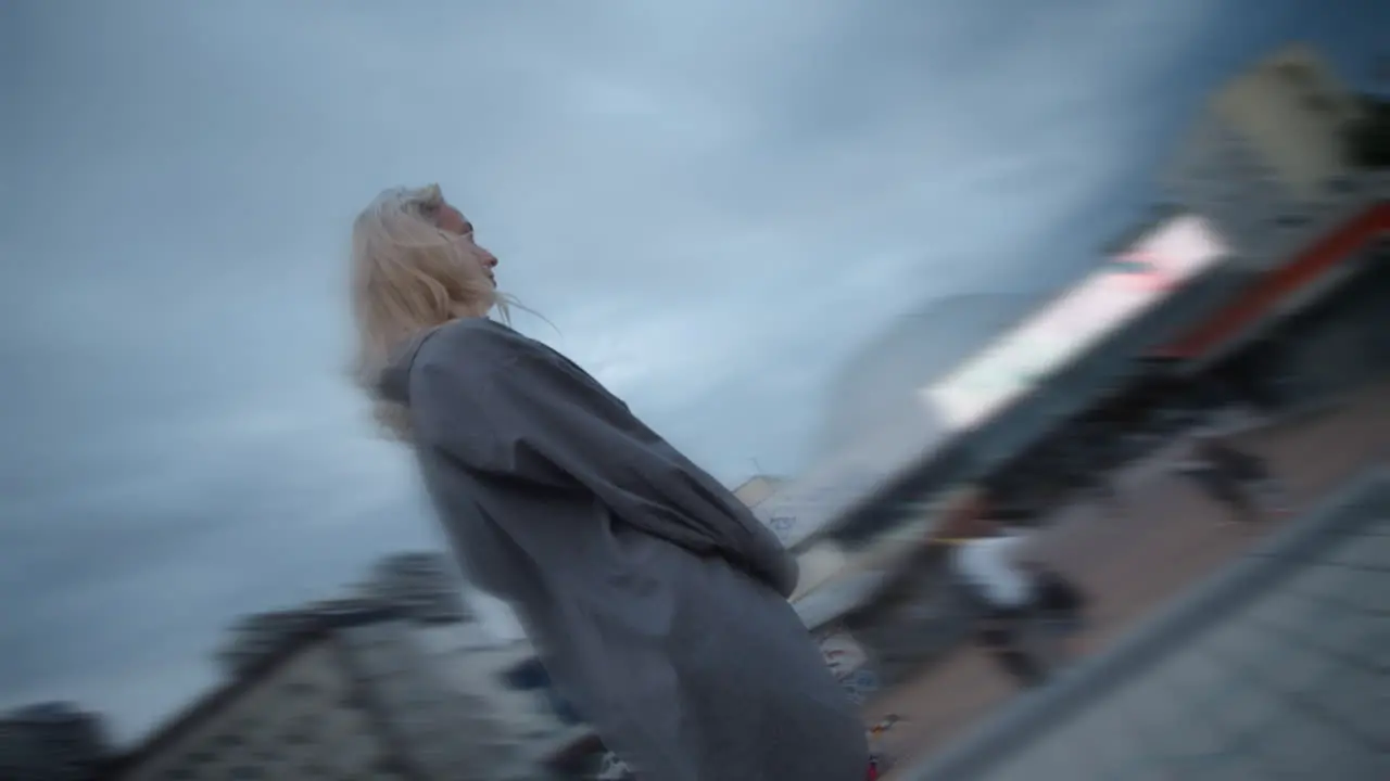 Blonde lady standing downtown of evening city with modern buildings