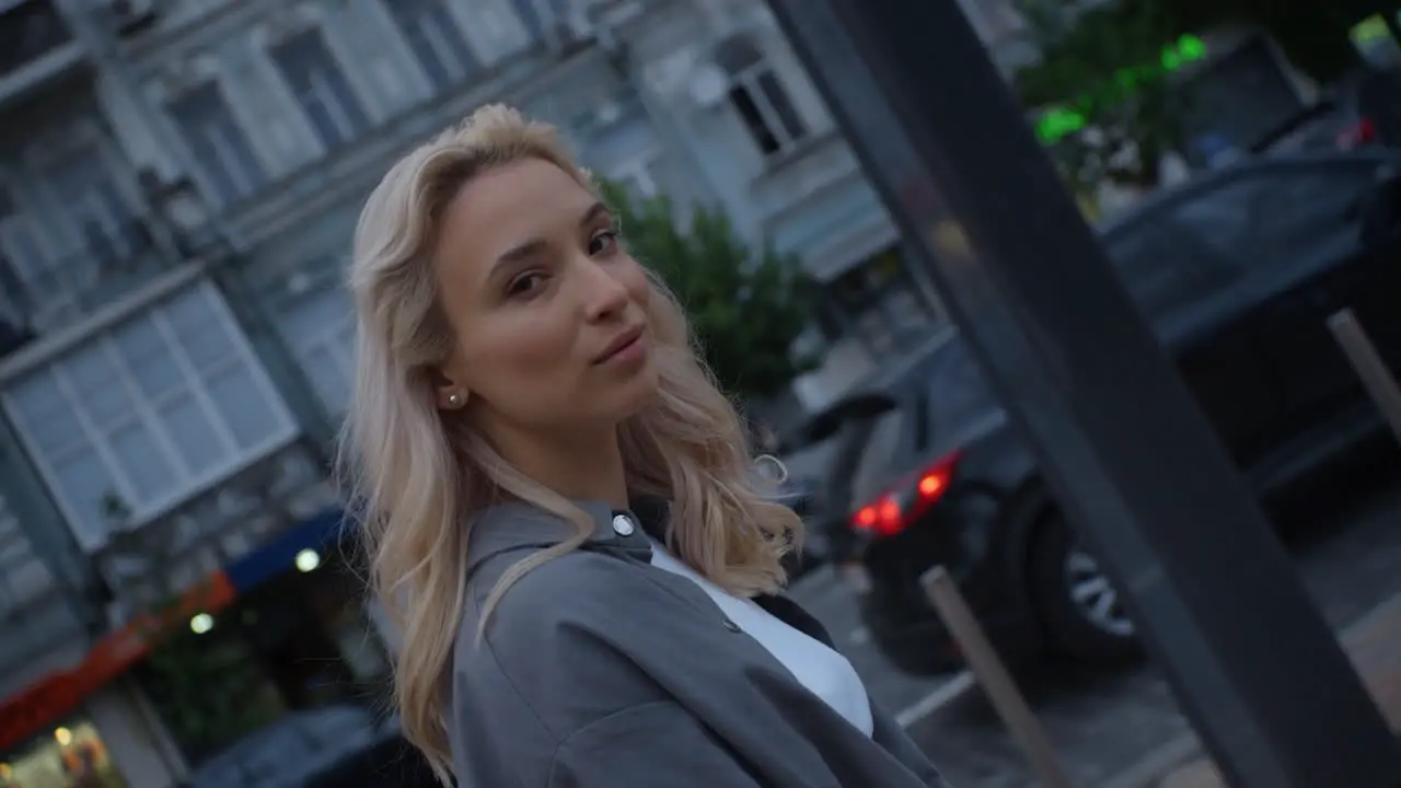 Blonde female model walking in evening city near road with driving cars