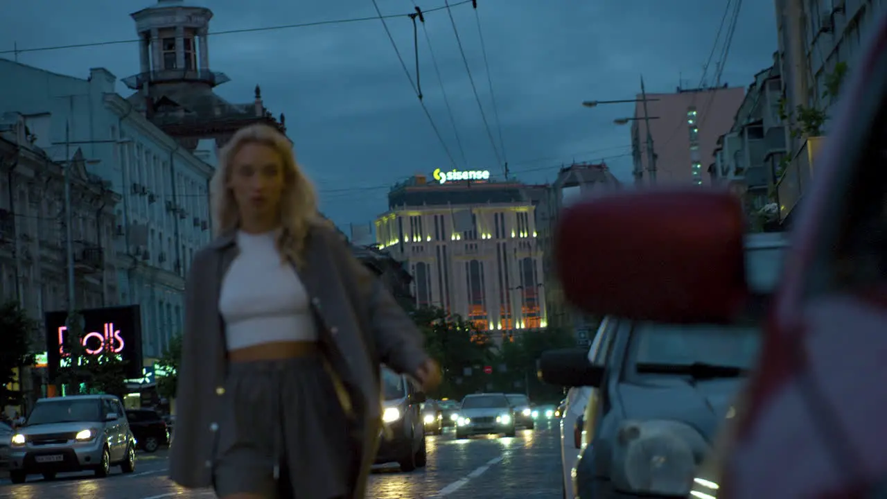 Female model walking towards camera at evening city traffic lights