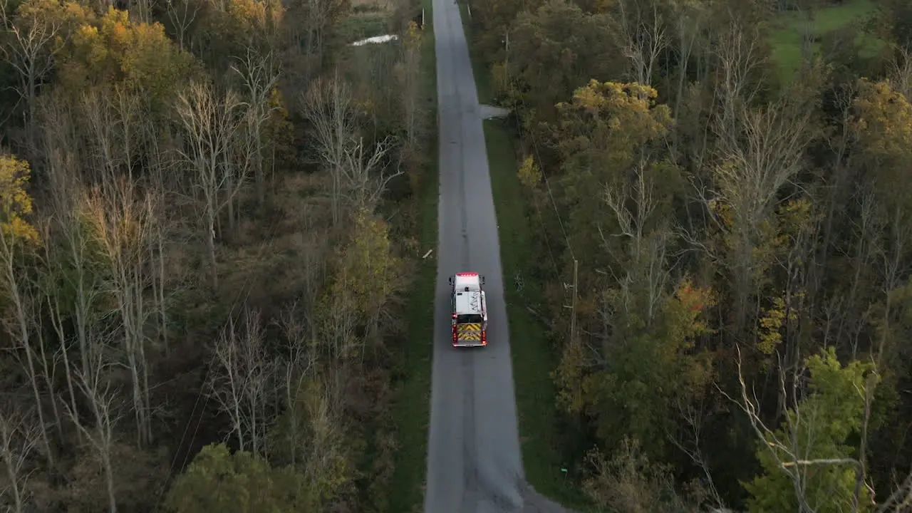 Aerial Tracking View of Emergency Fire Truck Vehicle Driving Moving Fast along Countryside Rural Road with Flashing Lights Rescue First Responder Mission for Fire Fighting Accident Alert