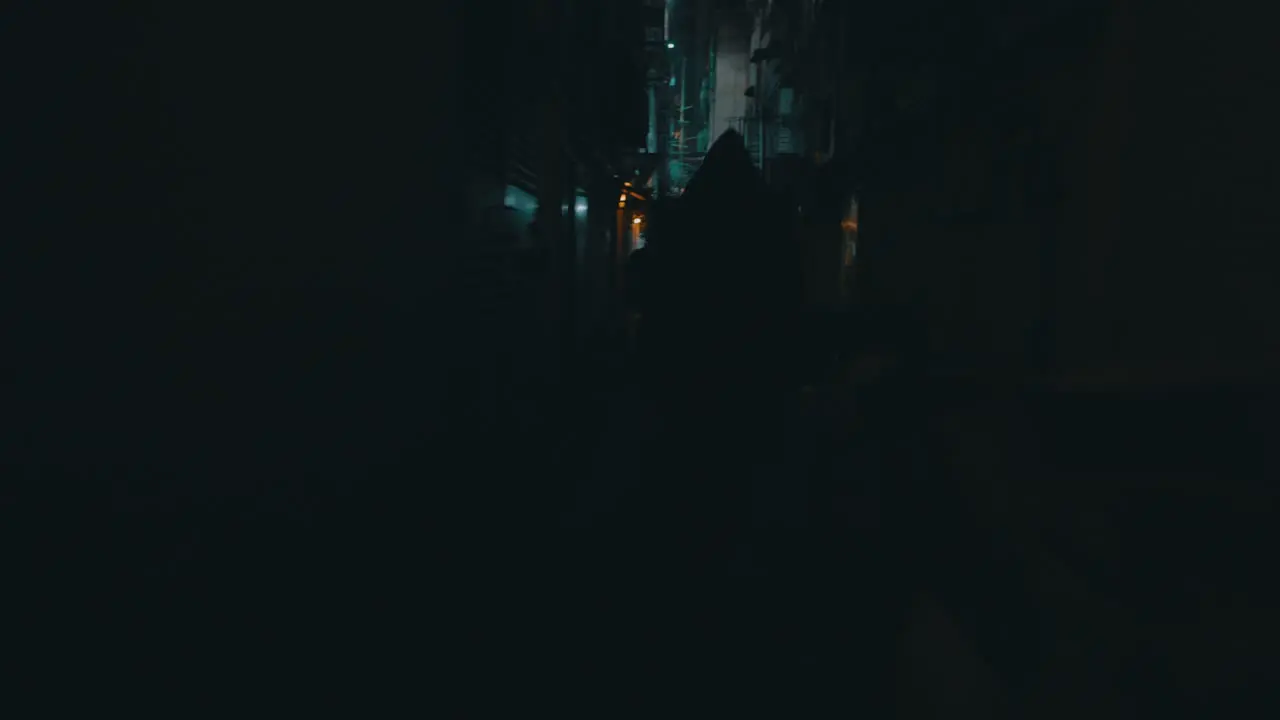 A cinematic shot of a hooded figure running behind a girl in a small dark eerie and dirty street during the night