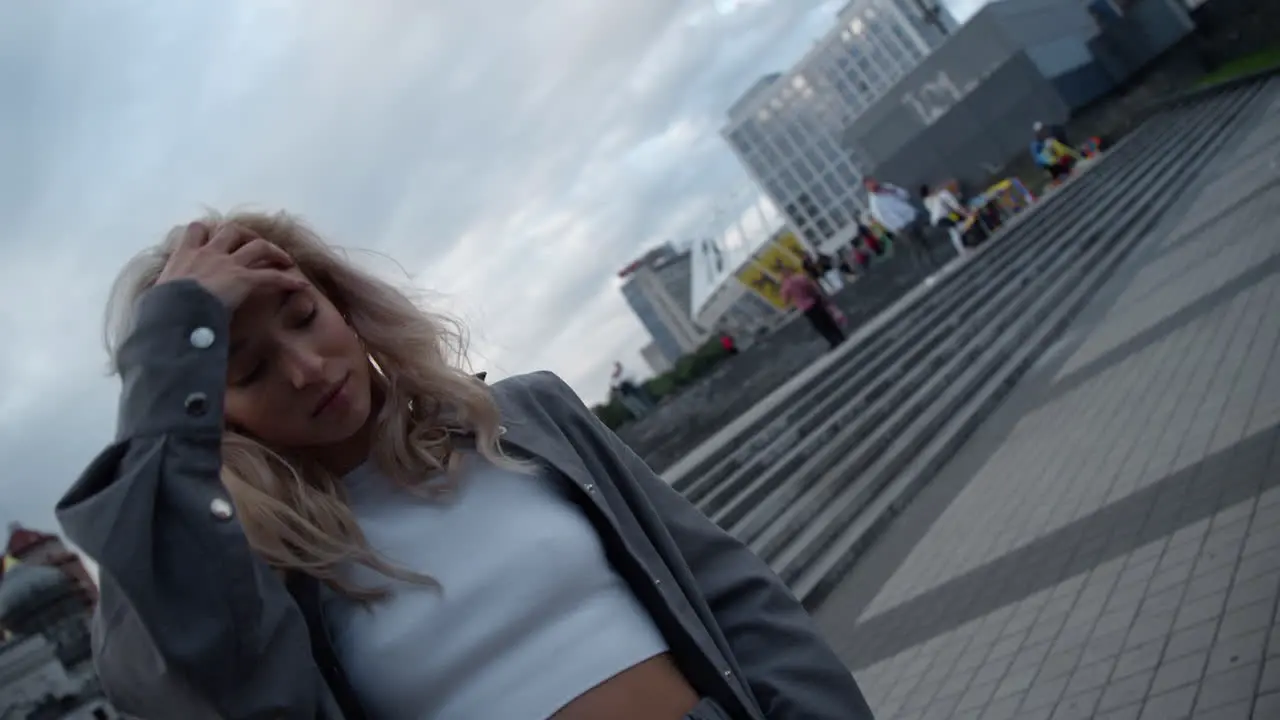 Cheerful woman touching hair in modern city buildings street