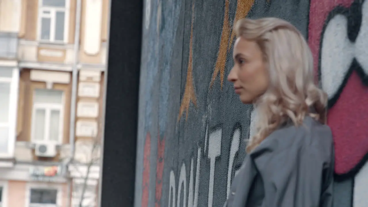 Blonde woman looking city view near graffiti wall on urban building