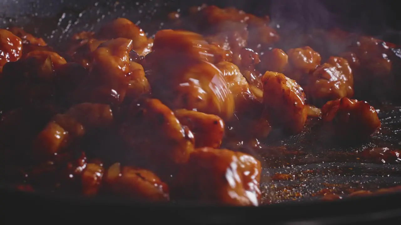 Mixing sweet and sour chicken with sauce in a frying pan using a wooden spoon close up view