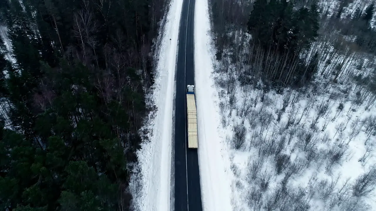 Aerial View Of Loaded Truck Driving On The Road Through Snowy Pine Forest In Winter