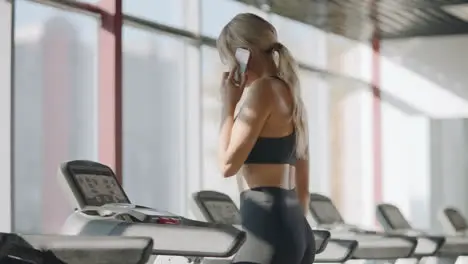 Fitness woman walking on treadmill in gym club Pretty girl calling mobile phone