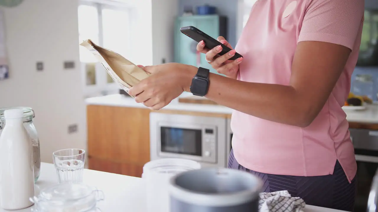 Woman Wearing Fitness Clothing Scanning QR Code On Food Packaging To Find Nutritional Information