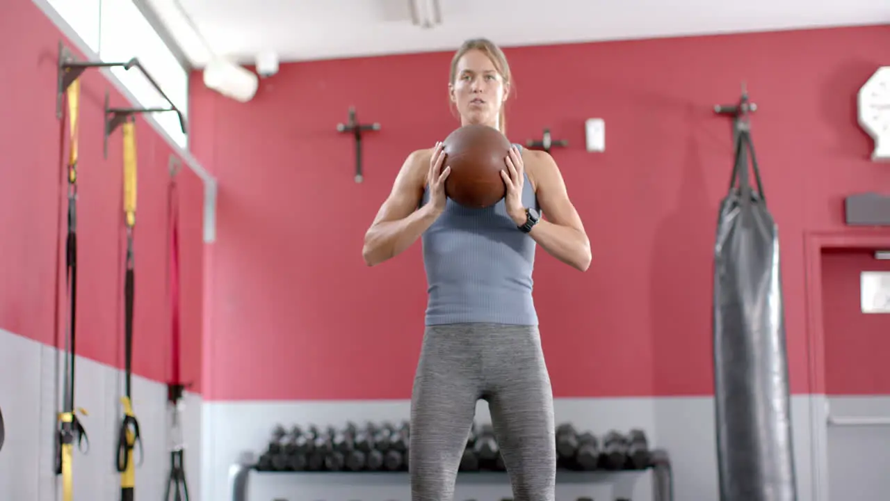 Fit young Caucasian woman squatting with a medicine ball at the gym