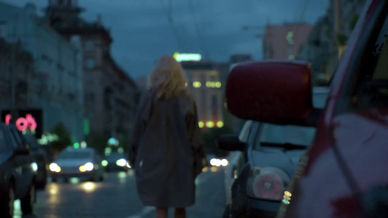 Woman going away evening city with cars passing on dark road lights