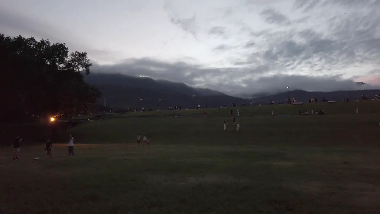 landscape green grass field with many people enjoying outdoor activities in sunset time