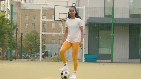 Portrait Of Young Woman With Football On Artificial Soccer Pitch In Urban City Area 