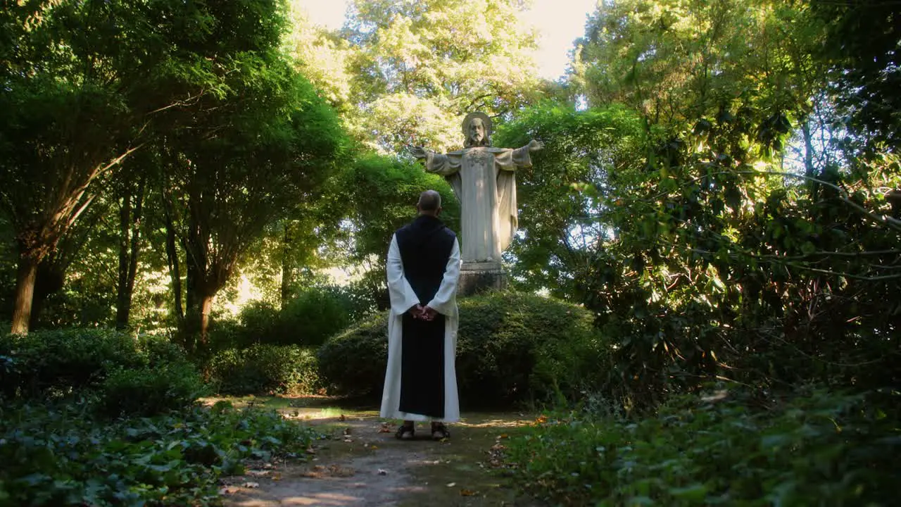 Amazing scene of a monk praying at a jesus statue surrounded with beautiful nature and trees