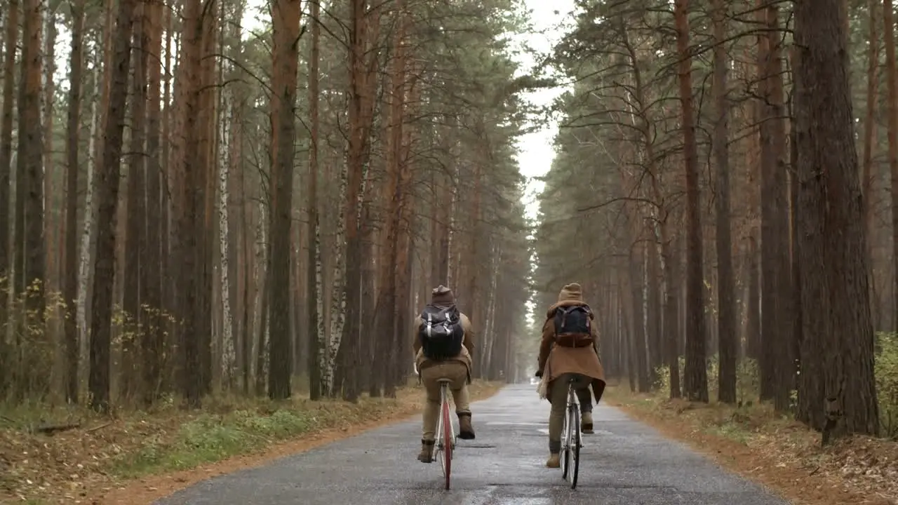 Rear View Of A Couple Wearing Winter Clothes Riding Bikes In The Forest While Raining 1