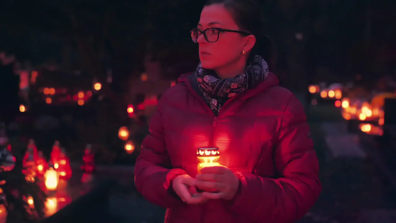 Woman visiting graveyard at night holding burning candle