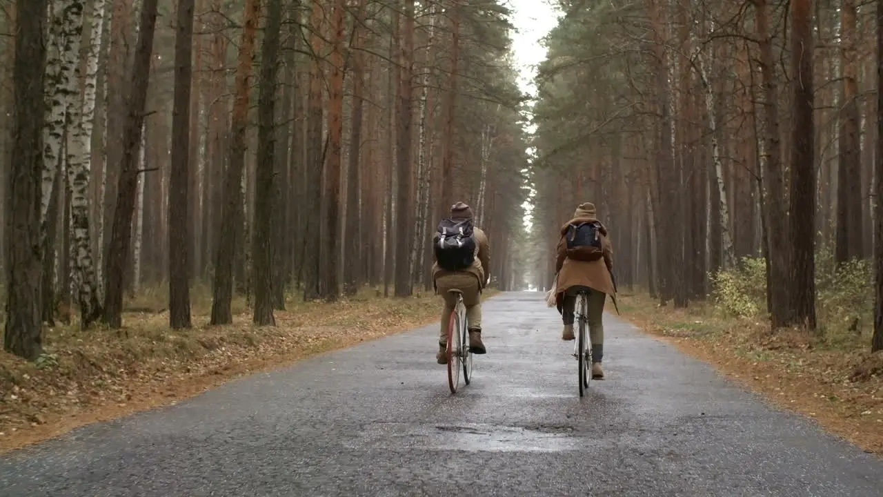 Rear View Of A Couple Wearing Winter Clothes Riding Bikes In The Forest While Raining