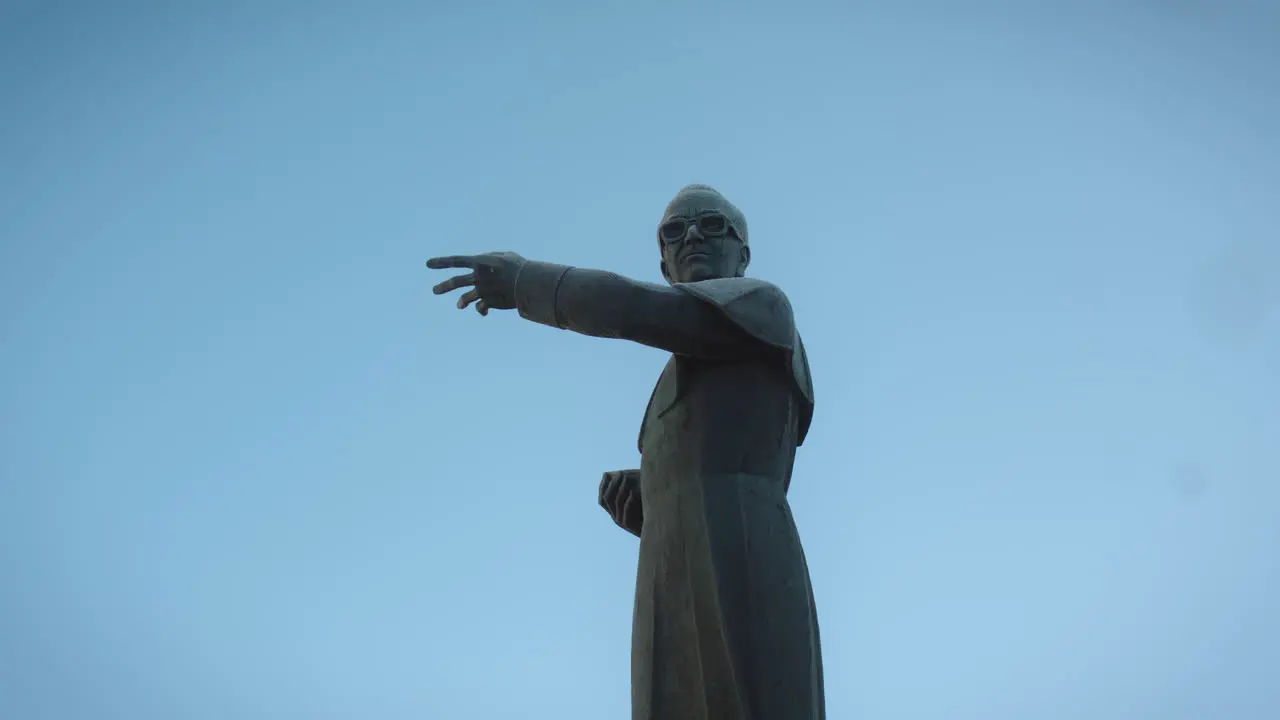 Low perspective camera shot of a statue of a priest who is pointing in one direction