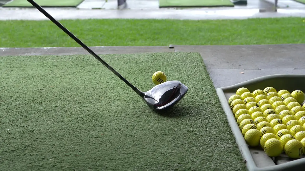 tray of balls and person hitting with a golf driver off the mat