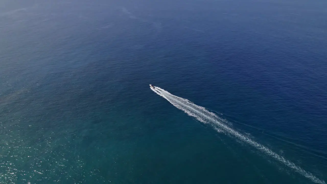 Lone motor boat speeds across blue water high angle drone tracking shot