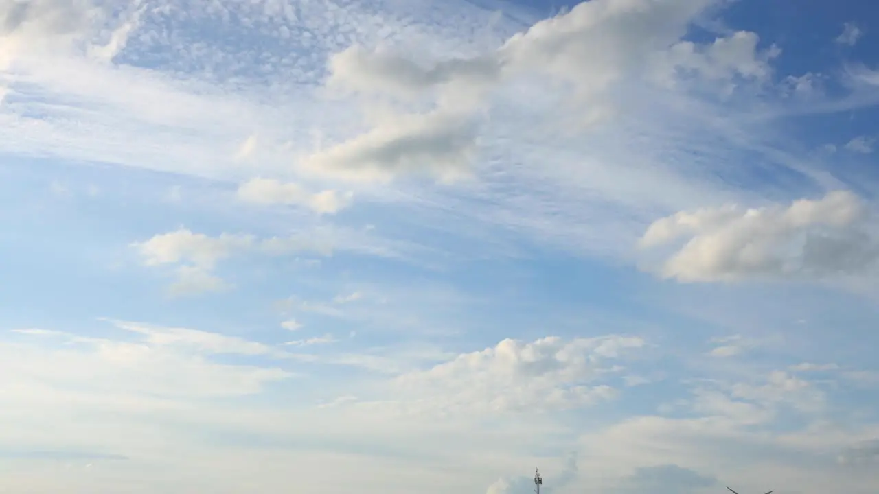 Calm cloud blanket forming and small cumulus clouds passing by with a blue sky and sun rays into sunset