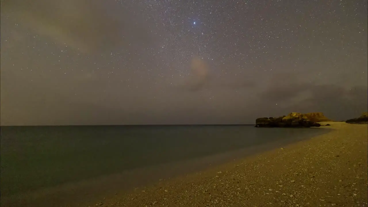 Arabian gulf starry night sky wonders in a dark sand beach in Persian sea with rocky mountain scenic shining blue phytoplankton and landscape of Traditional boat sailing concept and marine lifestyle