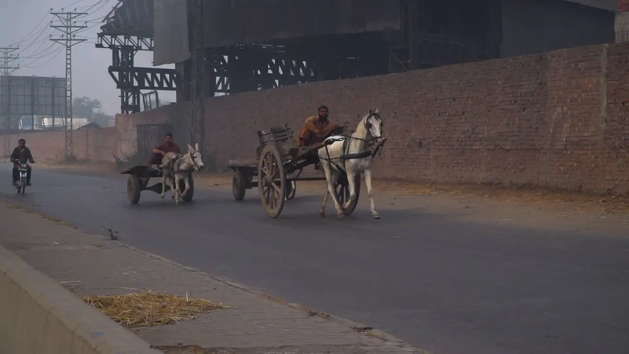 A horse cart two donkey cars and a motorcycle on the road in winters`s foggy season Electric polls wall sign board and a factory with the road