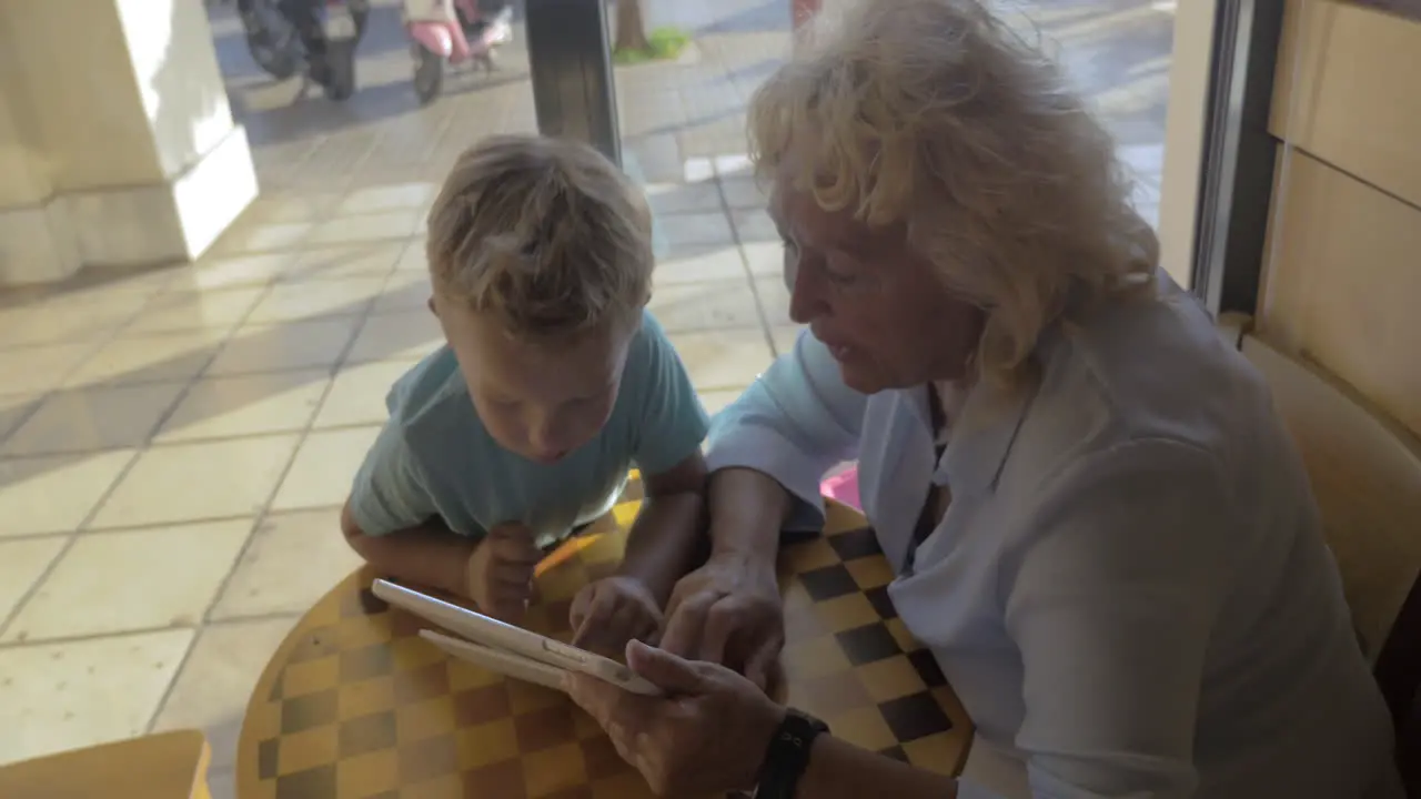 Child and grandma using tablet PC in cafe