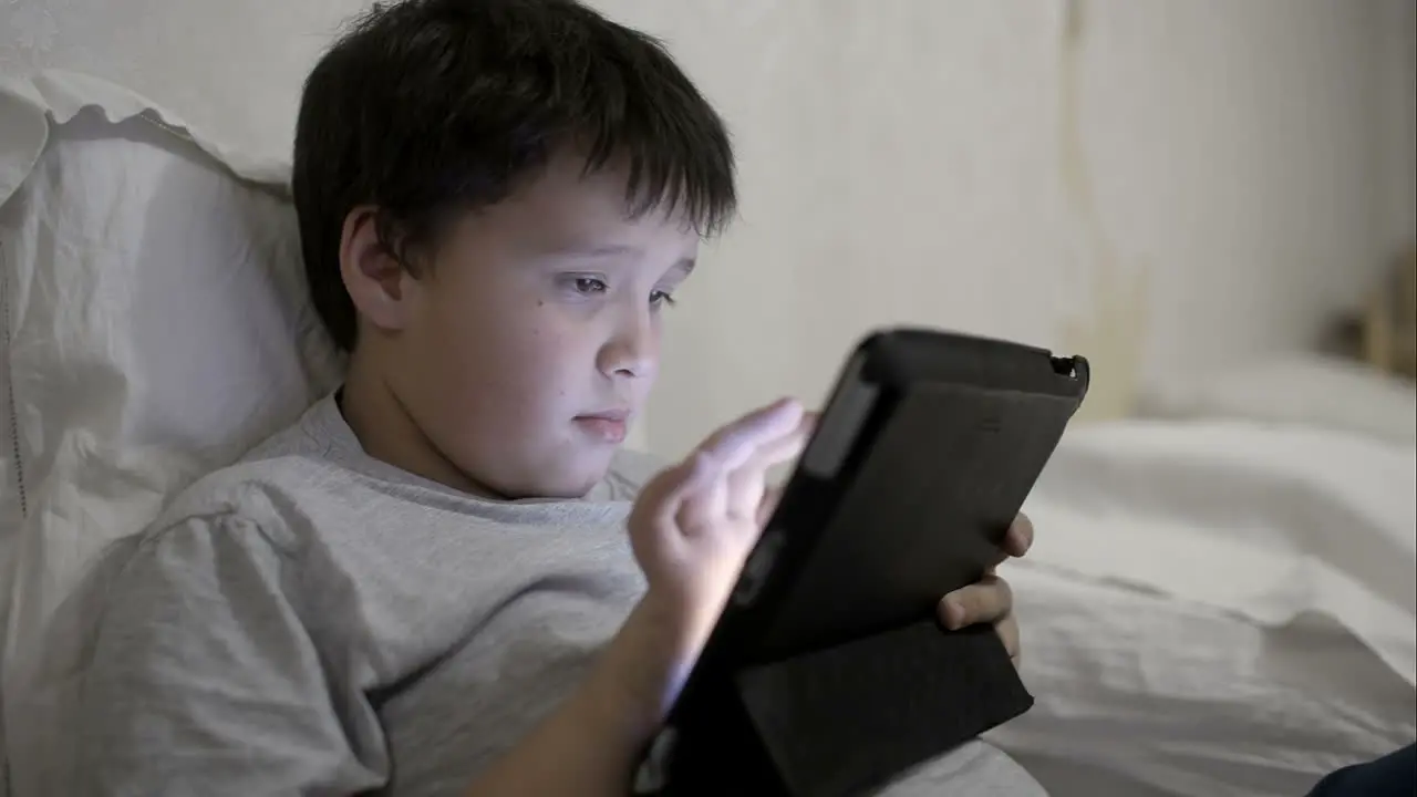 Teenager boy using tablet computer lying in bed