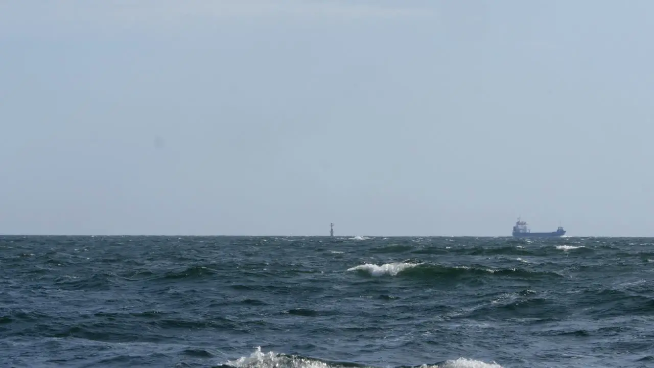 A lighthouse can be seen in the middle of the frame next to it a cargo ship slowly passes by