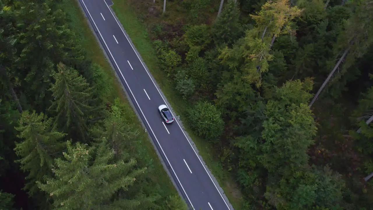 Aerial view following a electric SUV on a Swiss mountain forest road high angle drone shot