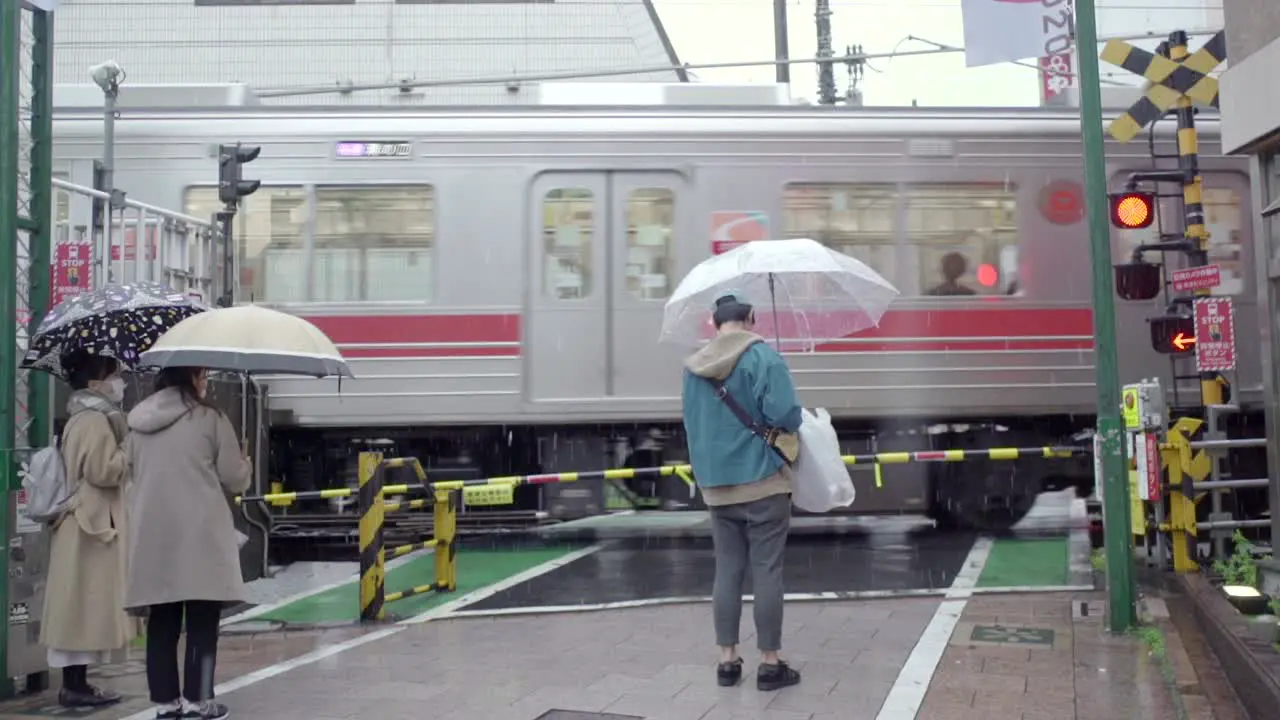 Japanese People With Umbrellas Waiting For The Train To Pass Through Before Crossing At The Railway In Tokyo Japan On A Rainy Day Tripod Slowmo Closeup