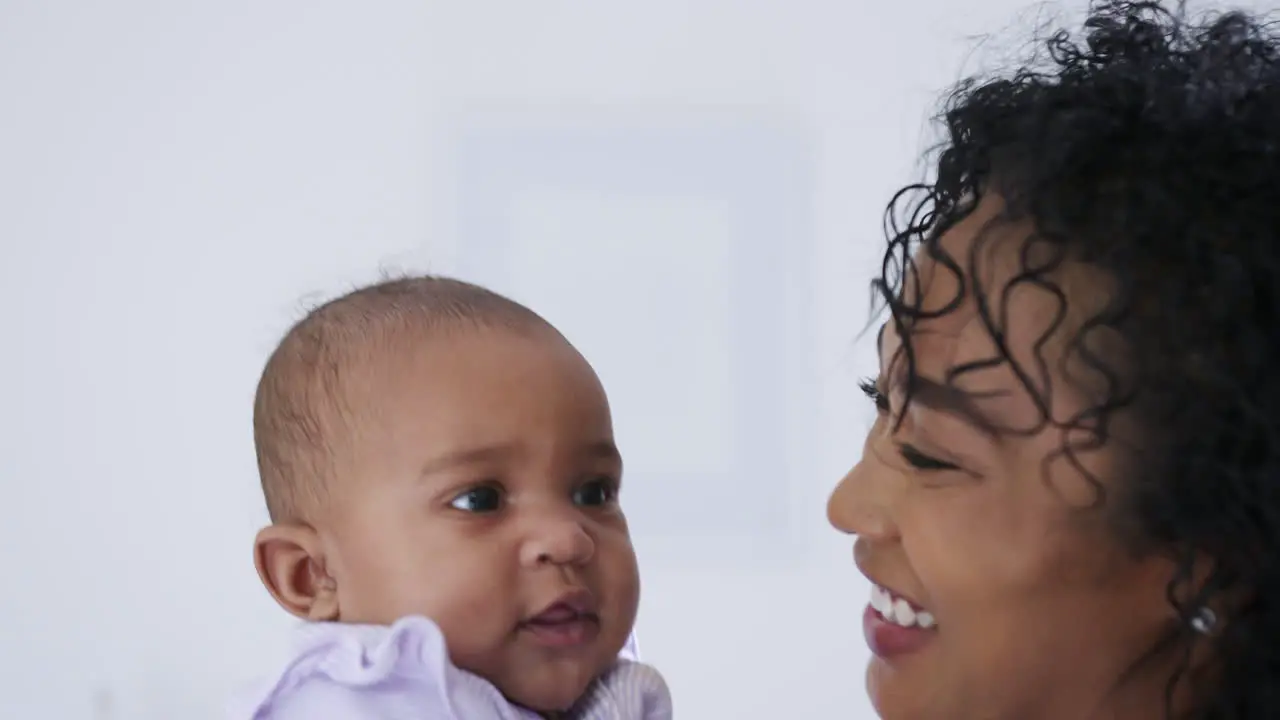 Loving African American Mother Wearing Pyjamas Playing With Baby Daughter In Bedroom At Home