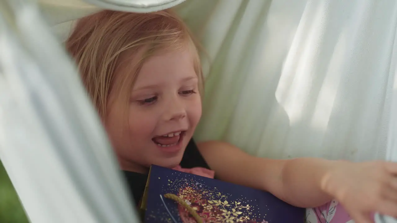 A happy little girl swings in the hammock holding a gift bag