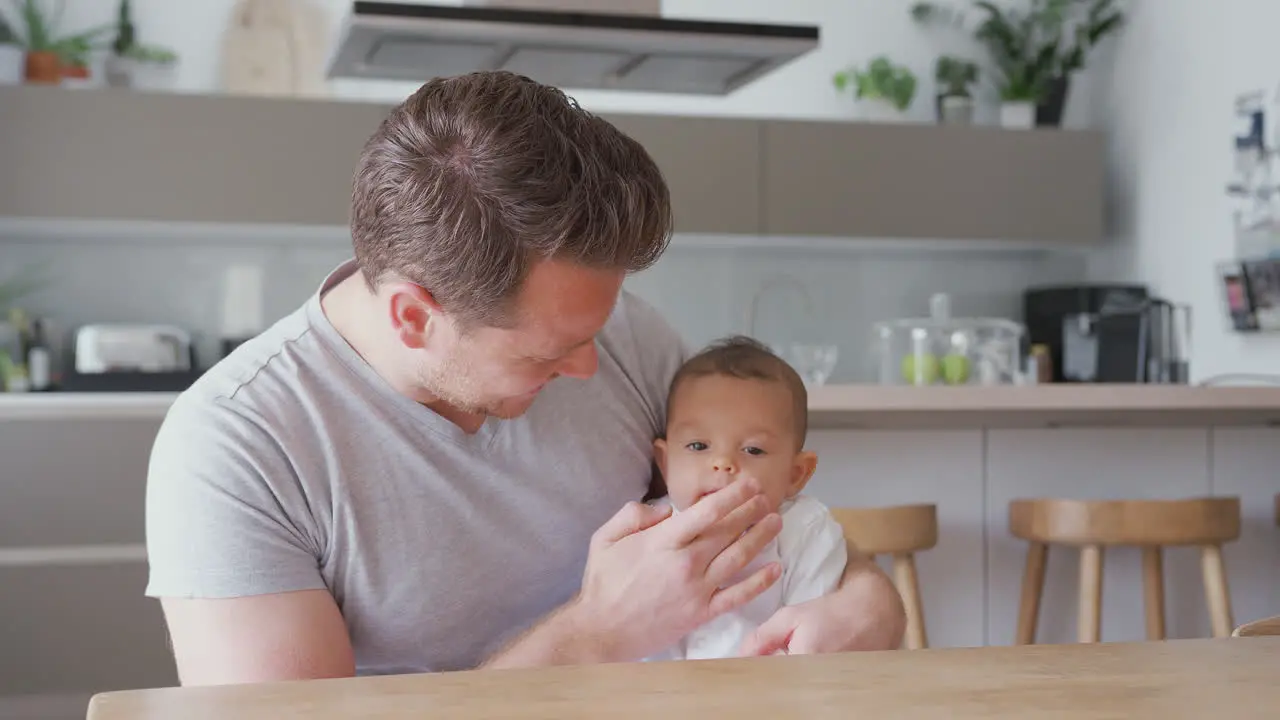 Loving Father Holding 3 Month Old Baby Daughter In Kitchen At Home