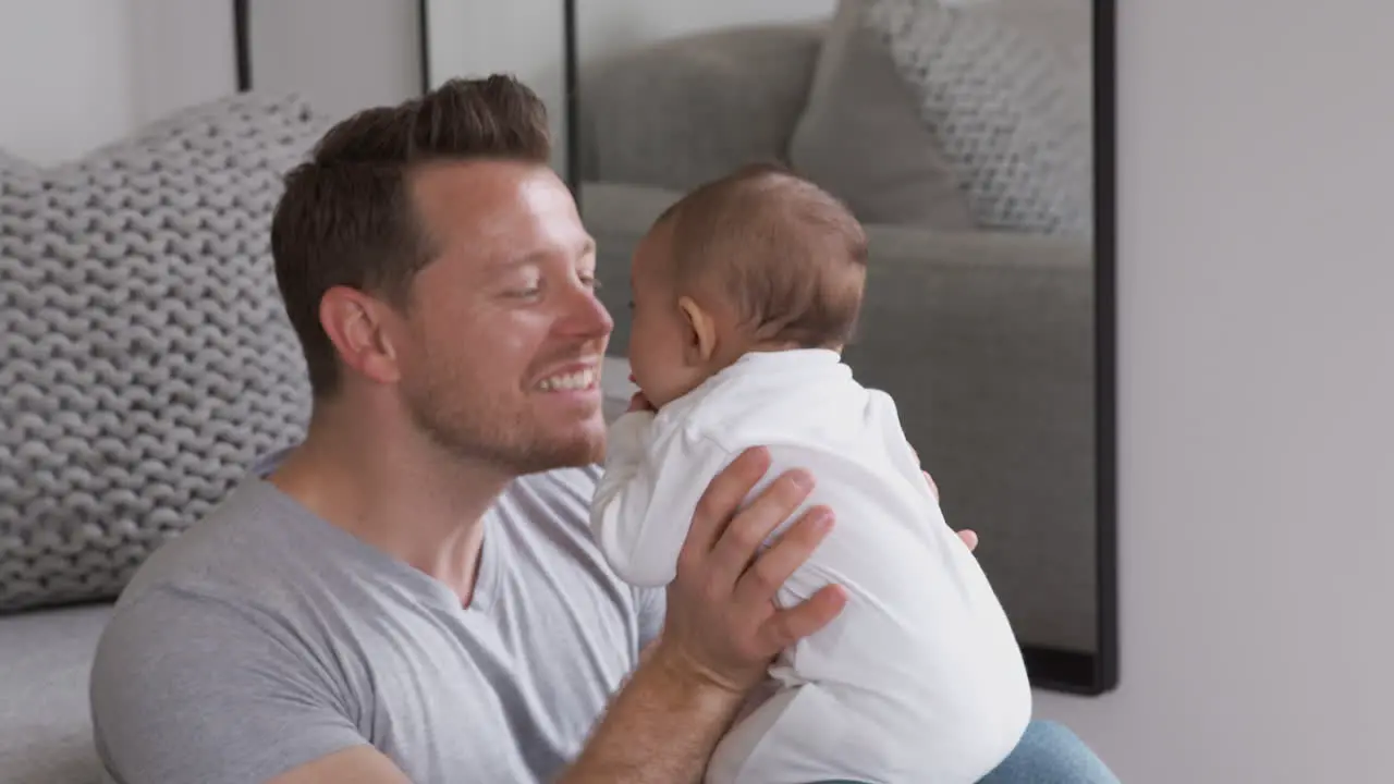 Father Holding Baby Daughter In The Air And Making Faces To Make Her Laugh