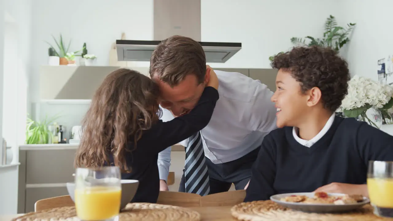 Daughter Helping Businessman Father To Put On Tie As Children Eat Breakfast In Kitchen Before School