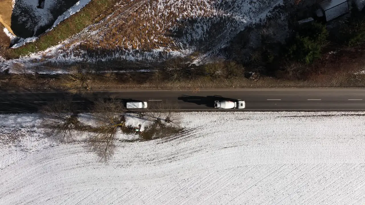 A driving concrete mixer vehicle passes the snowy landscape top down with slow zoom out